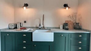 A kitchen with a central island, two wall-mounted lights, and a wooden floor. - Luxury hideaway in PDS - The Stonehouse Front Door (Saint-Jean-d'Aulps)