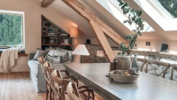 Ein gemütliches Loft mit Holztisch, Stühlen und einem großen Fenster mit Blick auf Grünflächen.