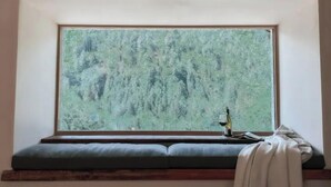 Ein Zimmer mit einem großen Fenster, einer fest eingebauten Sitzbank und einem kleinen schwarzen Gerät an der Wand.