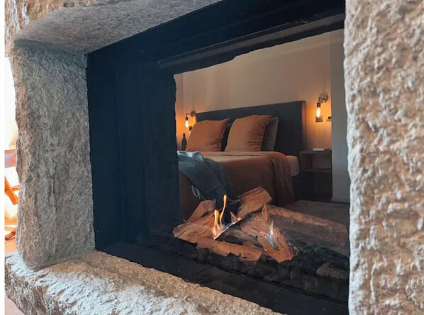 A stone fireplace with a bed and nightstand in the background.