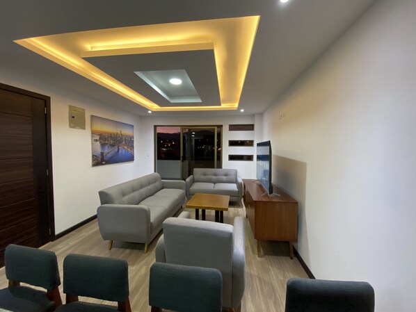 A modern living room with a sectional sofa, a TV, and a ceiling light fixture.