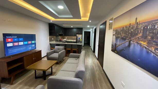 A modern living room with a flat-screen TV, grey sofas, a wooden coffee table, and a cityscape mural on the wall.