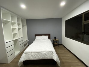 A bedroom with a bed, a wardrobe, a nightstand, and a large window.