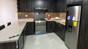 A modern kitchen with dark cabinetry, a stainless steel refrigerator, a built-in oven, and a granite countertop.