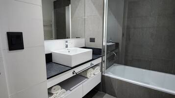 A modern bathroom with a white vanity, a glass shower enclosure, and a bathtub.