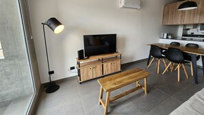 A modern living space with a wooden entertainment unit, a TV, a bench, and a dining area with chairs. - Loi Flats Neuquen, Edificio Talero (Neuquén)