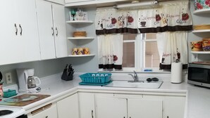 Una cocina con armarios blancos, cafetera, fregadero y microondas.
