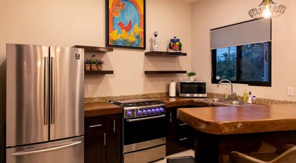 A modern kitchen with a stainless steel refrigerator, a built-in oven, a microwave, and a gas stove. There is a window providing natural light and a painting above the counter. - Stand Alone 2-Bedroom Villa / Private Pool / Todos Santos,Short walk to Downtown (Todos Santos)