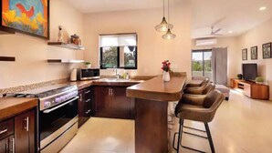 Une cuisine moderne dotée d’un îlot central, d’un coin repas avec des tabourets de bar, d’un téléviseur et d’un ventilateur de plafond.