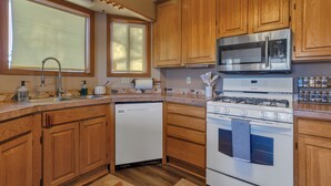 Une cuisine dotée de meubles en bois, d’un four à micro-ondes en acier inoxydable, d’un lave-vaisselle et d’une cuisinière à gaz.