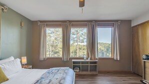 Une chambre à coucher avec un grand lit, une table de chevet avec une lampe, une commode en bois et une fenêtre avec des rideaux.