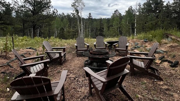 Un foyer entouré de fauteuils Adirondack, situé dans une zone boisée.