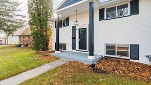 Ett modernt hus i två våningar med vit fasad, svarta fönsterluckor och en veranda på framsidan.