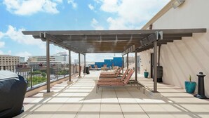Una terraza en la azotea con pérgola, sillones de descanso y una parrilla.