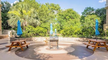 An outdoor patio with a barbecue grill, picnic tables, and blue umbrellas.