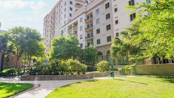 A multi-story residential building with balconies, surrounded by well-maintained greenery and a stone pathway.