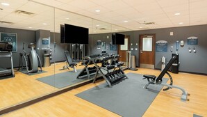 Un gimnasio con equipo de ejercicio, espejos y carteles informativos.