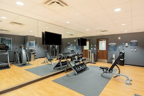 Un gimnasio con equipo de ejercicio, espejos y carteles informativos.