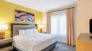 A hotel room with a large bed, two bedside tables with lamps, a flat-screen TV, a painting on the wall, and a window with curtains.