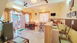 A spacious living area with a dining table, multiple chairs, ceiling fans, and a television. - Hotel Madhuvan (Kandaghat)