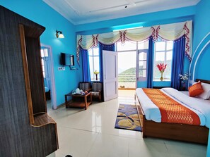 Una habitación de hotel con una cama grande, un escritorio con silla, un televisor y un balcón con cortinas.