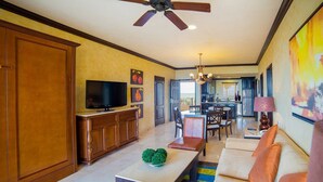 A spacious living room with a sofa, coffee table, and television. There is a kitchen area in the background with a dining table and chairs. - Cancun 5 stars Luxury Resort and Spa, 1 bedroom suite, 2 baths, sleep 4 (Punta Sam)