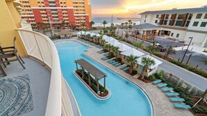 Zona de piscina en un resort con piscina curvo, sillas de descanso y vista al océano al atardecer.
