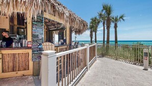 Un bar junto a la playa con techo de paja, barandilla de madera y una pizarra con el menú.