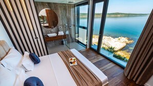 A modern bedroom with a large bed, a bathroom with a mirror and sink, and a view of the sea.