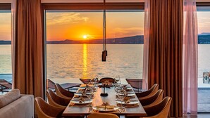 A dining table set for six with a view of the sunset over the water.