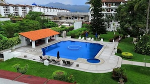 A swimming pool with lounge chairs, surrounded by well-maintained lawns and a building with a red-tiled roof.
