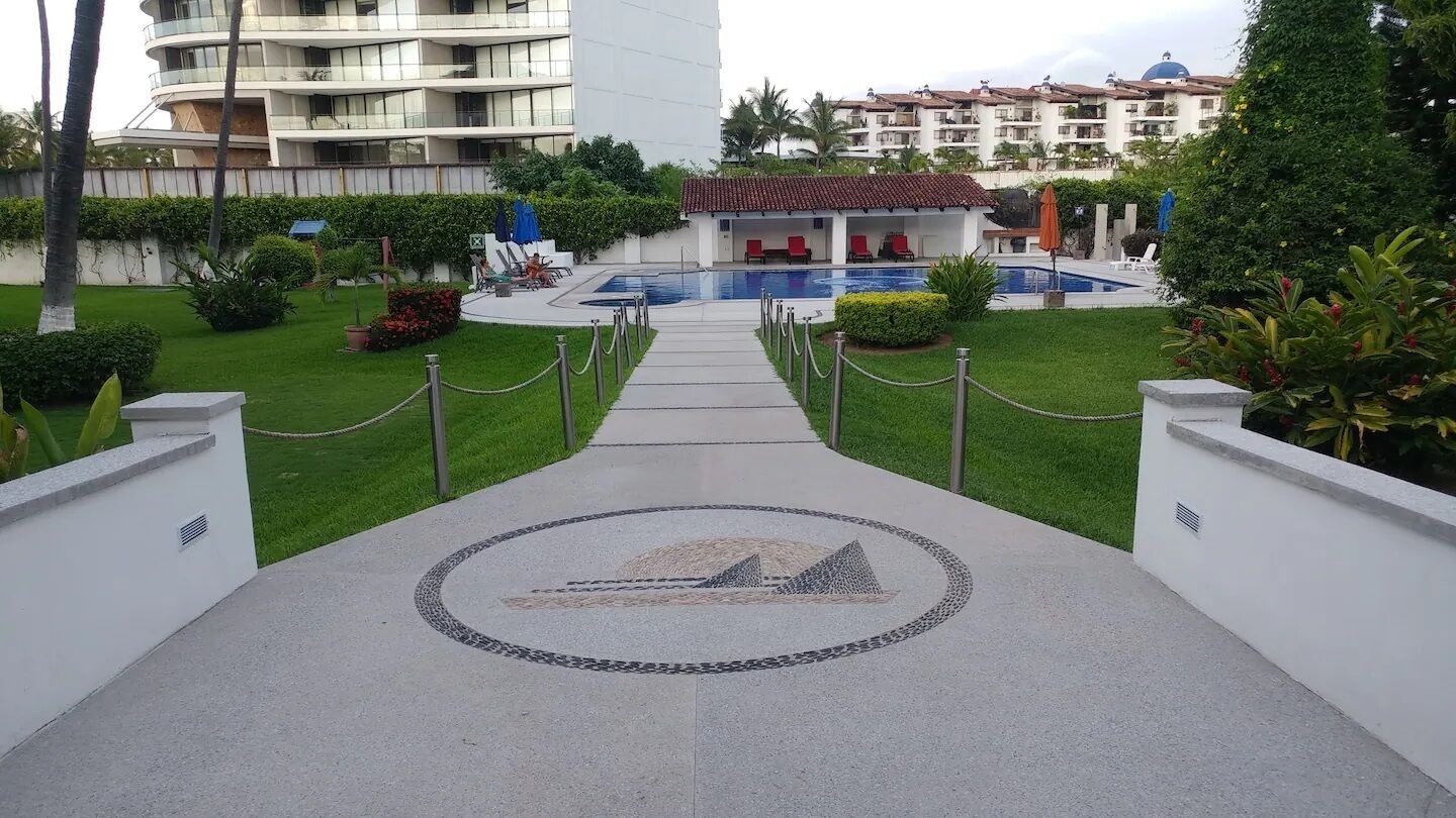 Ein Hotel Eingangsbereich mit Poolanlage, überdachter Sitzgelegenheit und einem Weg zum Pool.