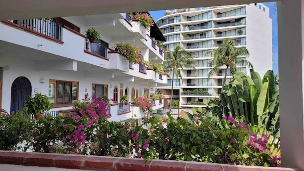 A multi-story hotel with balconies, potted plants, and a view of palm trees.
