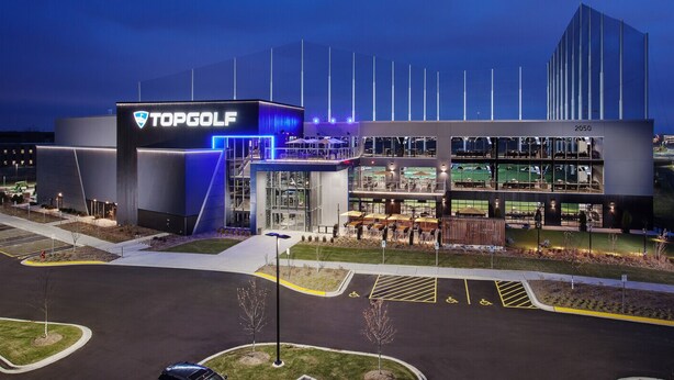 Un complex modern de Topgolf amb una entrada destacada, diversos nivells i una zona d'aparcament.