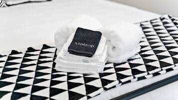 Una cama bien hecha con una funda de almohada a cuadros blanco y negro y una toalla doblada con la etiqueta 'Maquillaje'.