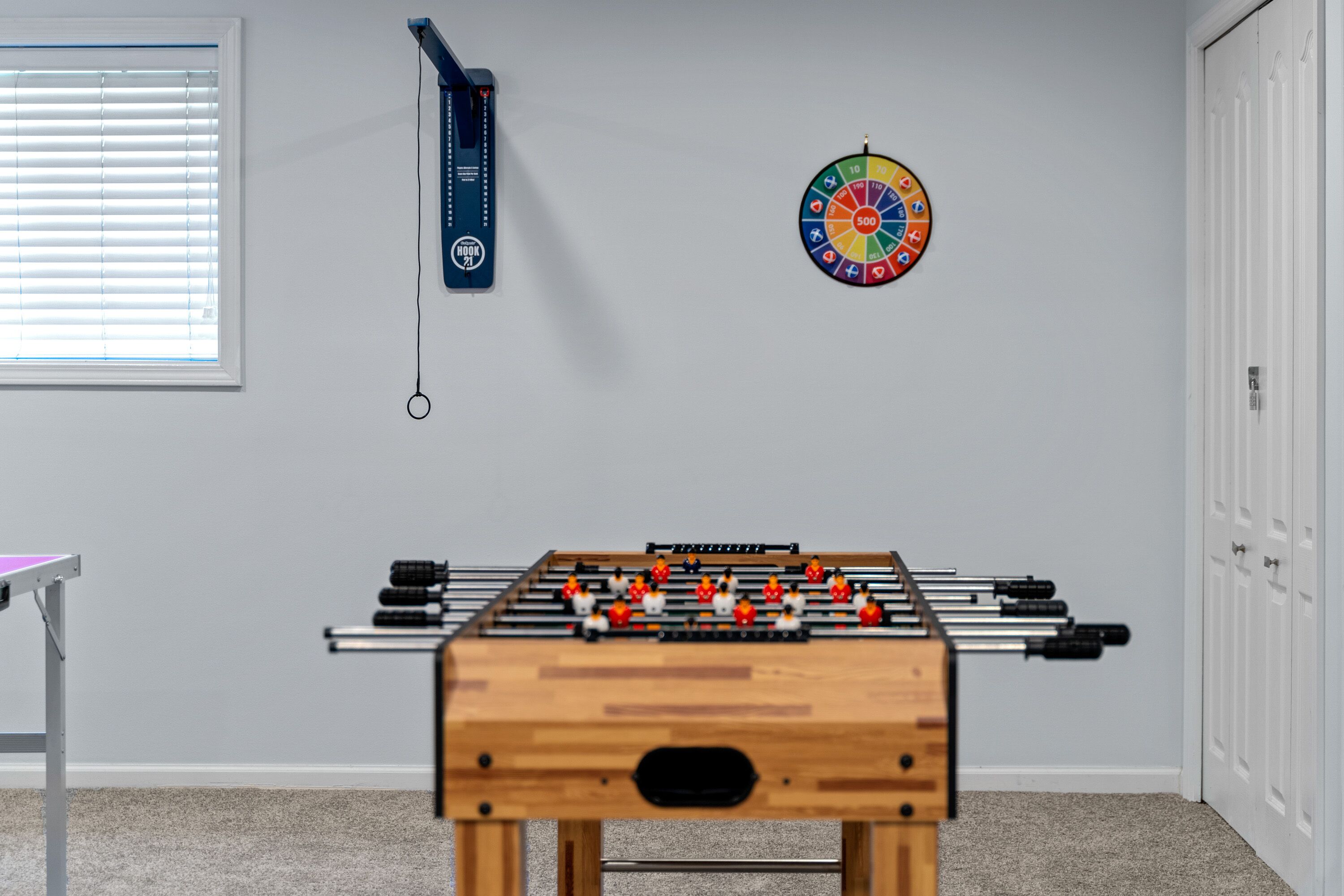 A room with a foosball table, a dartboard, and a wall-mounted exercise device.