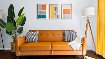 Quarto com um sofá de couro marrom, uma planta grande em vaso e três obras de arte abstratas emolduradas na parede.