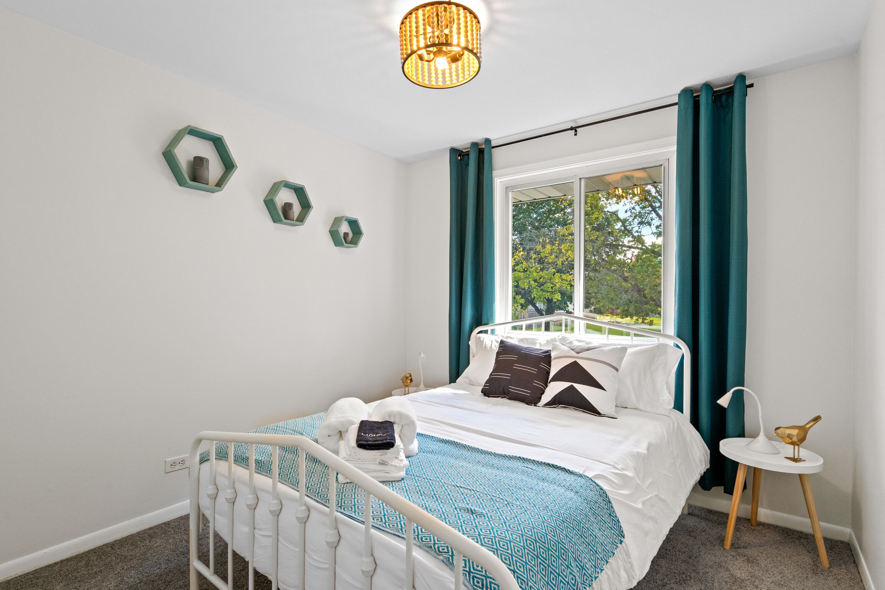 A neatly arranged bedroom with a bed, a bedside table with a lamp, and a window with curtains.