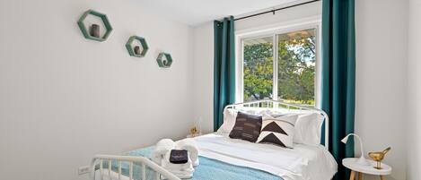 A neatly arranged bedroom with a bed, a bedside table with a lamp, and a window with curtains.