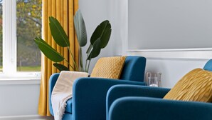 Habitació amb un sofà blau, una cortina groga i una planta.