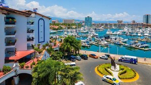 A marina with numerous boats docked, a roundabout, and a multi-story building with balconies. - CONDO MR BY TRVL2HM (Puerto Vallarta)