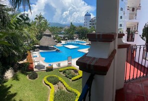 Ein Resort mit großem Schwimmbad, Palmen und einem strohgedeckten Gebäude.
