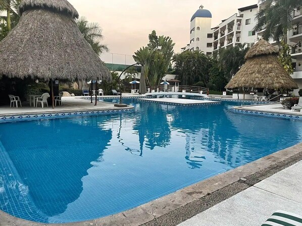 Ein Swimmingpool mit Reetsonnenstühlen, Liegestühlen und einem Gebäude mit Kuppel in der Ferne.