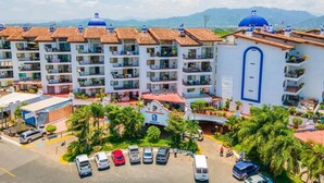 A multi-story hotel with balconies, a parking area, and a view of the mountains. - CONDO MR BY TRVL2HM (Puerto Vallarta)
