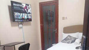 A hotel room with a bed, a chair, a TV mounted on the wall, and a door. - DALM-D Cozy lovely studio with Gym in Kileleshwa (Nairobi)
