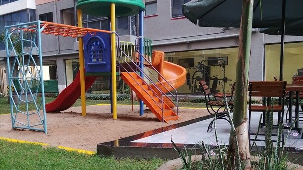 A playground with a slide and climbing structures, surrounded by a landscaped area with a planter and grass. - DALM-D Cozy lovely studio with Gym in Kileleshwa (Nairobi)