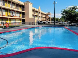 A swimming pool with a red border, surrounded by a fence, and a building with balconies in the background. - Ashland Studio Inn By OYO Richmond North near Kings Dominion (Ashland)