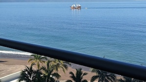 A view of a calm sea with a boat carrying passengers, a beach with palm trees, and distant mountains.