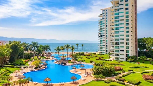 A resort with a large swimming pool, palm trees, and a tall hotel building. - CONDO SHAGUI BY TRVL2HM (Puerto Vallarta)