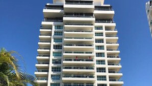 A multi-story hotel with balconies, a clear sky, and surrounding greenery. - CONDO SHAGUI BY TRVL2HM (Puerto Vallarta)